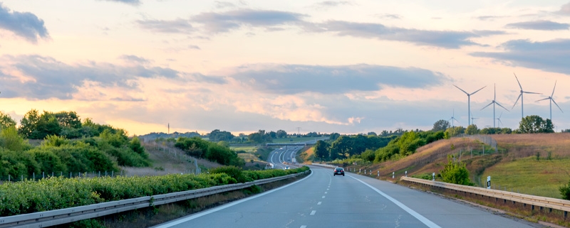 Carretera abierta en Cantabria al atardecer con paisaje verde y aerogeneradores, ideal para conducción segura con neumáticos en buen estado